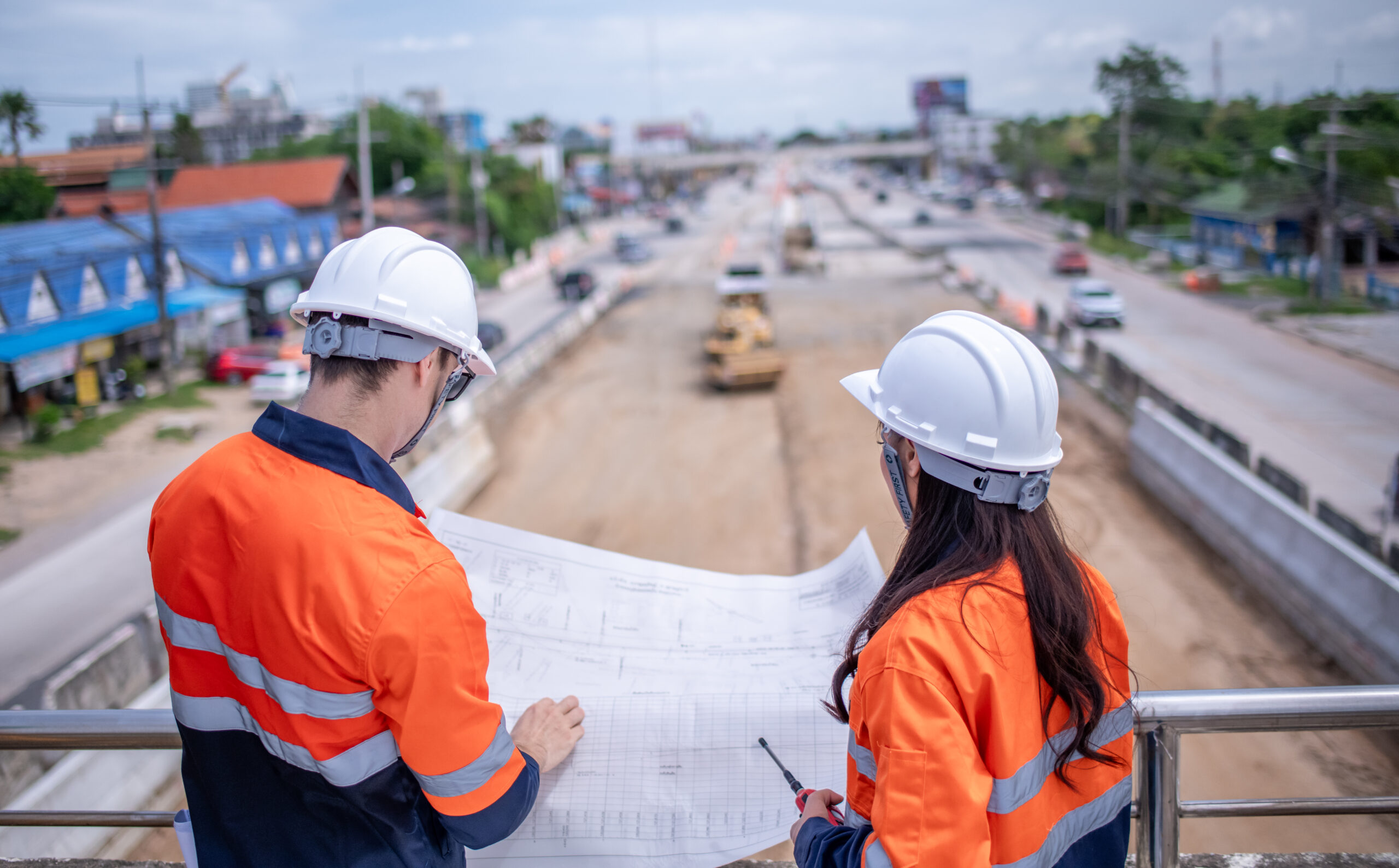 Engineers review blueprints over a highway roadwork site, showing construction equipment rental support